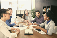 A diverse group of professionals engaged in a discussion around a conference table in a modern office setting.